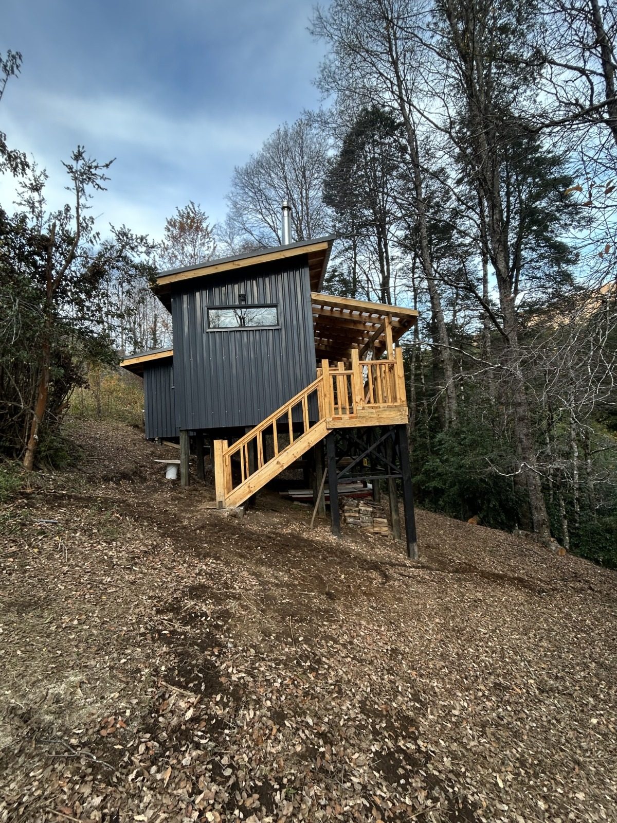 Refugio Mateo, cabaña de madera oscura sobre pilotes con escalera y terraza